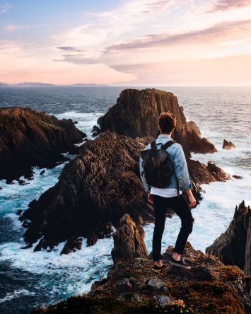 Guy standing on rocks looking out to the ocean Traveling on a Budget