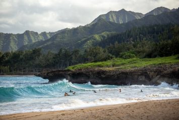 People swimming near the shore on one of Hawaii's islands with the view of volcanic mountains in the back.