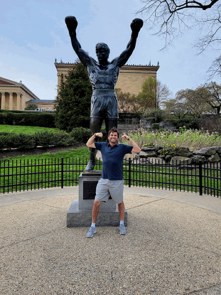 David Lieber in Philadelphia infront of the Rocky Balboa Statue flexing his muscles.
