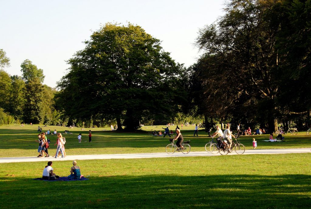 People in a park sitting down on the grass and riding bicycles
