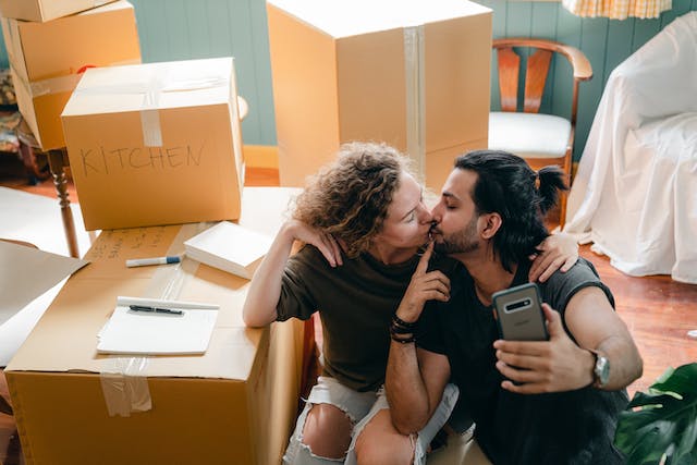Couple taking a selfie next to a pile of moving boxes and turning the stress of relocation into an adventure